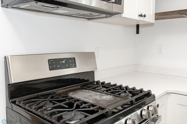 kitchen with stainless steel gas range, white cabinetry, and range hood