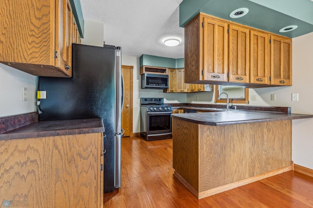 kitchen with stainless steel appliances, sink, kitchen peninsula, a textured ceiling, and wood-type flooring