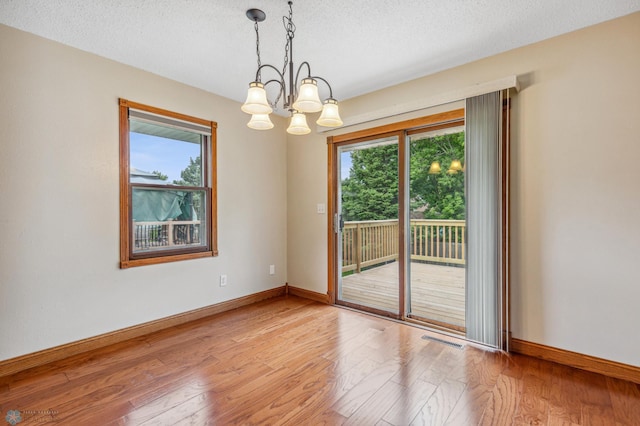 unfurnished room with a textured ceiling, a notable chandelier, and light hardwood / wood-style floors