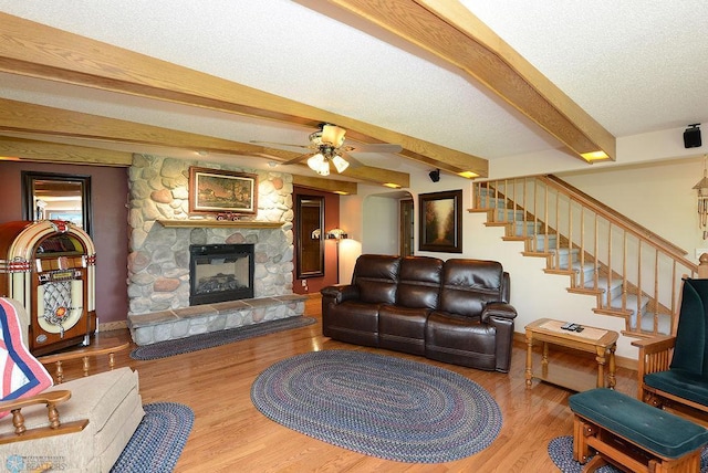 living room featuring a fireplace, wood-type flooring, ceiling fan, beam ceiling, and a textured ceiling