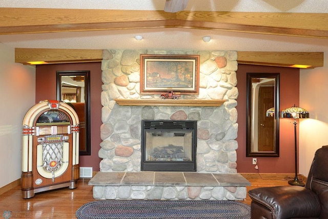 living room featuring beam ceiling, a stone fireplace, and hardwood / wood-style floors