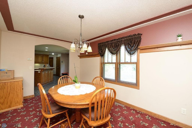 dining area featuring dark carpet, a textured ceiling, ornamental molding, and a notable chandelier