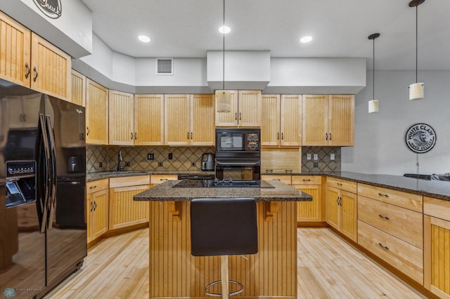 kitchen featuring light wood-type flooring, black appliances, backsplash, and a breakfast bar