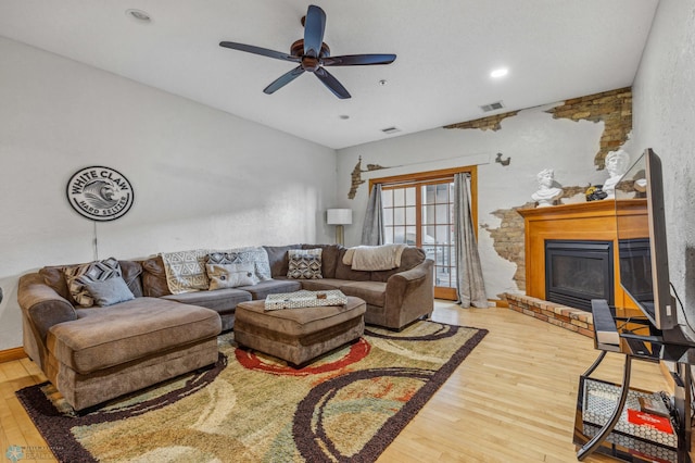 living room with a fireplace, light wood-type flooring, and ceiling fan