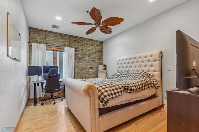 bedroom with ceiling fan, brick wall, and light hardwood / wood-style flooring