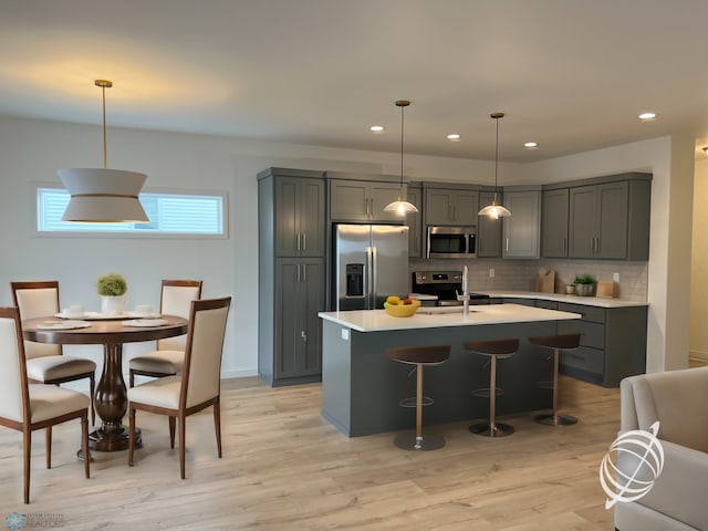 kitchen featuring tasteful backsplash, stainless steel appliances, a center island with sink, pendant lighting, and light hardwood / wood-style floors