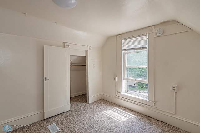 unfurnished bedroom with multiple windows, a closet, vaulted ceiling, and light colored carpet