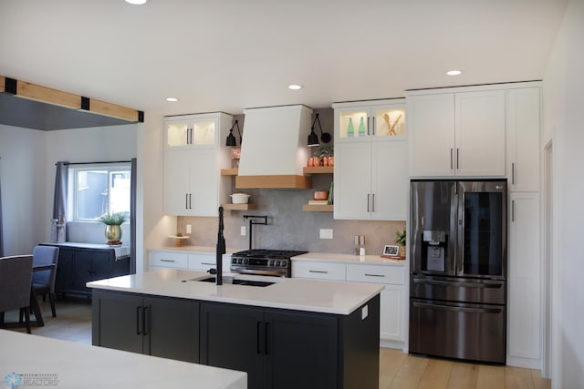 kitchen featuring a center island with sink, premium range hood, backsplash, refrigerator with ice dispenser, and white cabinetry