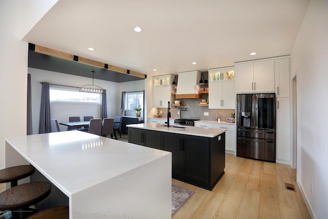 kitchen featuring an island with sink, white cabinets, and fridge with ice dispenser