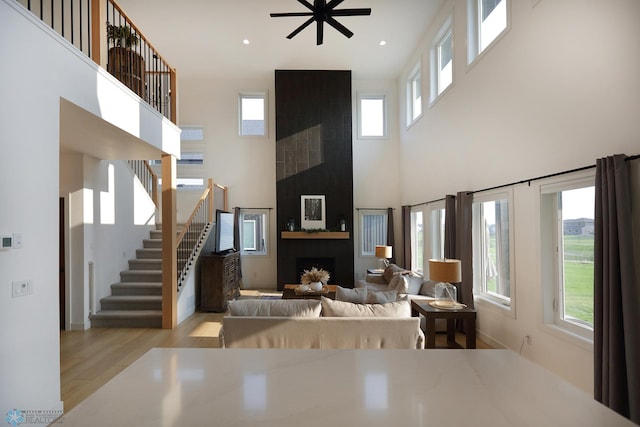 living room featuring light wood-type flooring, a fireplace, plenty of natural light, and a towering ceiling