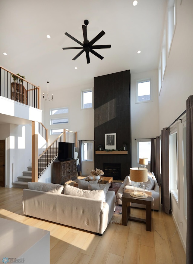 living room featuring ceiling fan with notable chandelier, light wood-type flooring, and a large fireplace