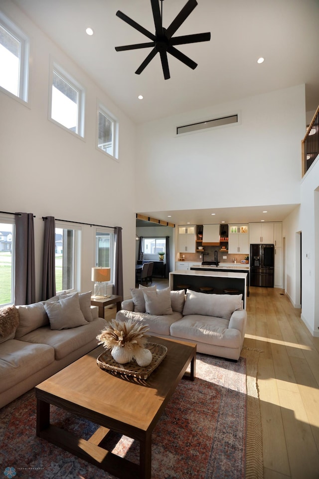 living room with sink, light hardwood / wood-style flooring, ceiling fan, and a high ceiling