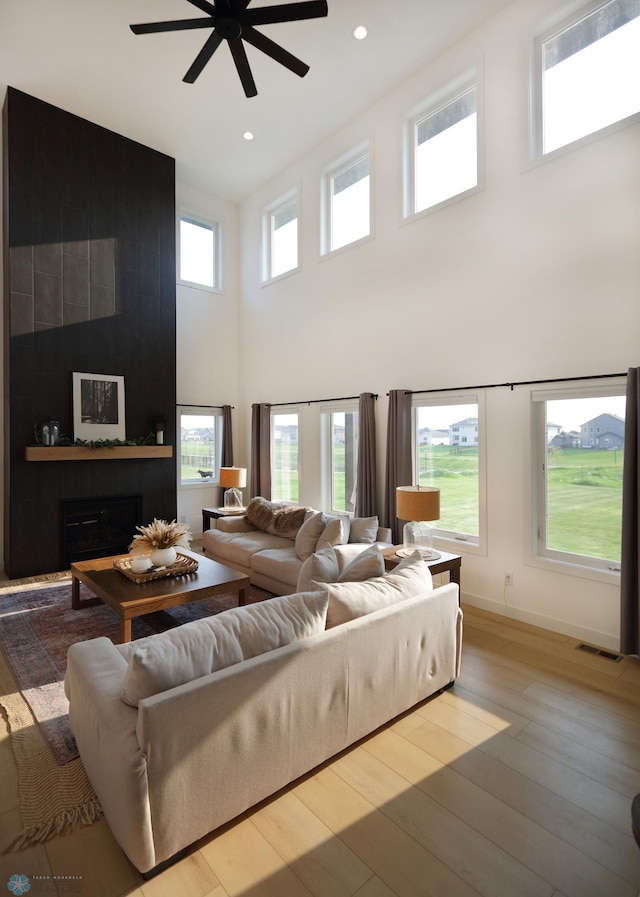 living room with ceiling fan, a fireplace, hardwood / wood-style flooring, and a towering ceiling