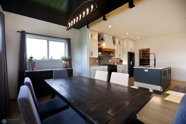 dining room with sink, light wood-type flooring, and beam ceiling