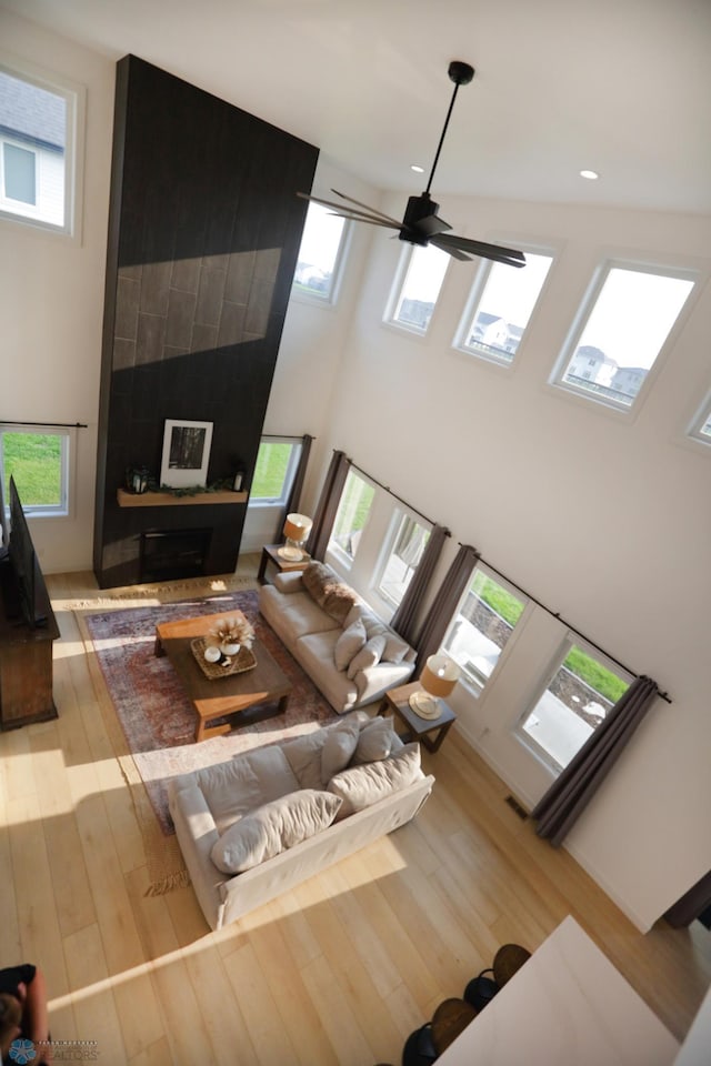 living room featuring a tiled fireplace, hardwood / wood-style flooring, a towering ceiling, and ceiling fan