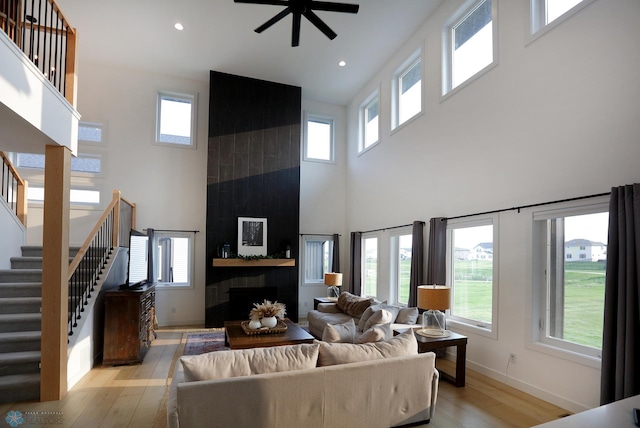 living room with light hardwood / wood-style floors, a fireplace, ceiling fan, and a high ceiling