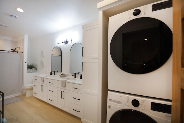 laundry room featuring stacked washing maching and dryer, sink, and light hardwood / wood-style flooring