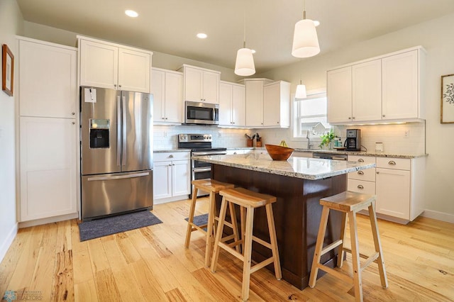 kitchen featuring a breakfast bar area, light wood-type flooring, white cabinets, a center island, and appliances with stainless steel finishes