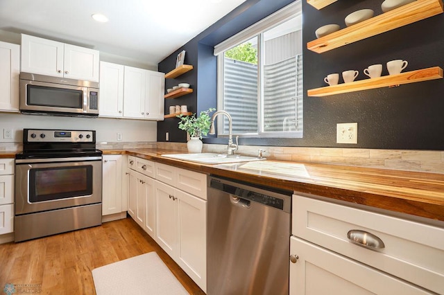 kitchen with wood counters, stainless steel appliances, white cabinets, sink, and light hardwood / wood-style floors