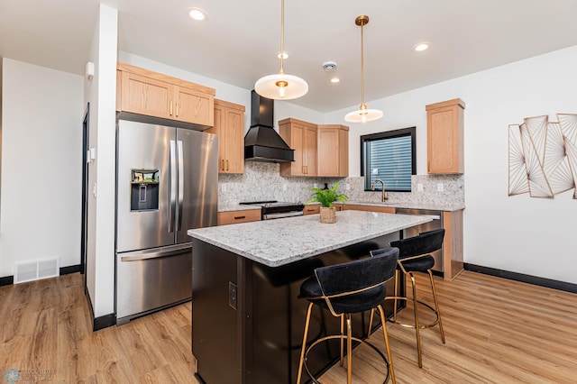 kitchen with custom exhaust hood, a kitchen island, stainless steel appliances, light brown cabinetry, and light hardwood / wood-style floors