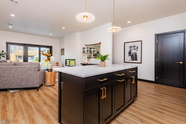 kitchen with light stone counters, a kitchen island, decorative light fixtures, and light hardwood / wood-style flooring