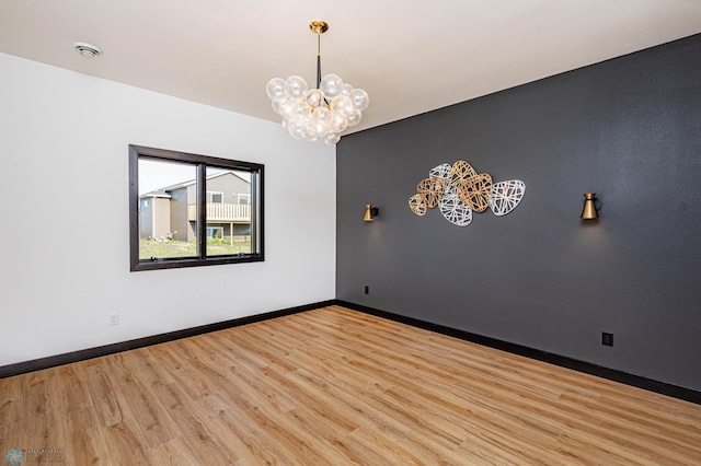 empty room with light wood-type flooring and a notable chandelier