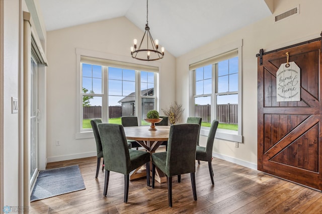 dining space with vaulted ceiling, a barn door, a wealth of natural light, and hardwood / wood-style floors