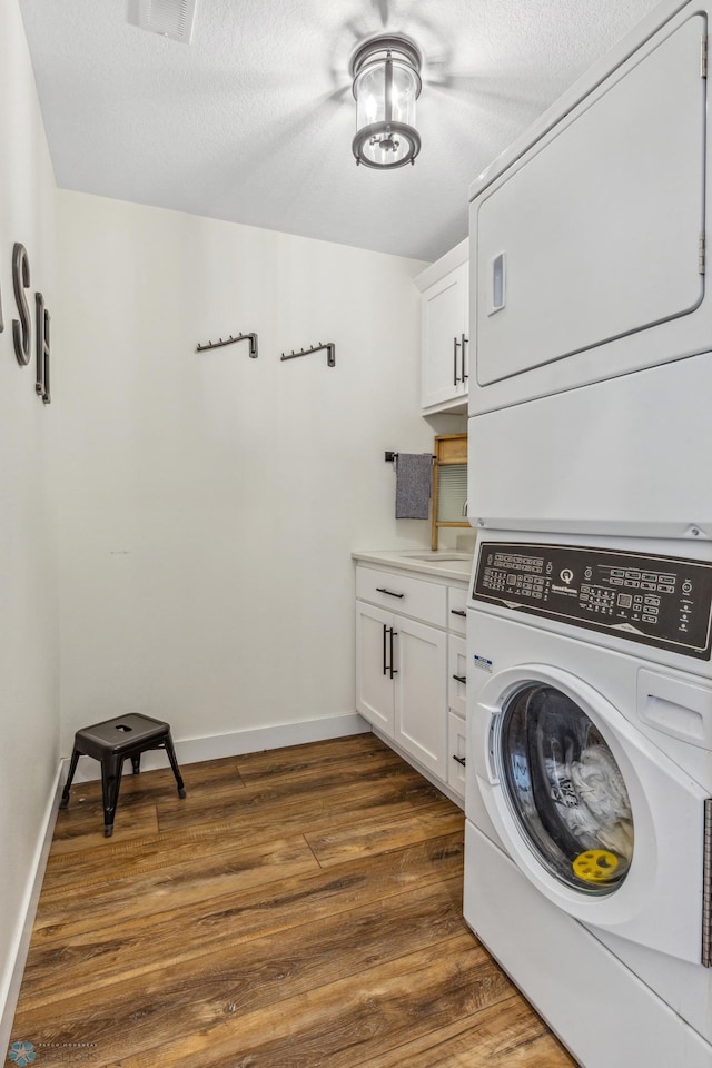 clothes washing area with a textured ceiling, dark hardwood / wood-style floors, cabinets, and stacked washer / drying machine