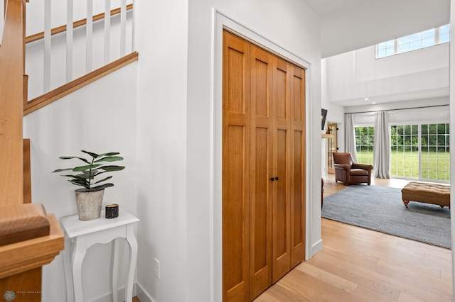 hall featuring light wood-type flooring and a towering ceiling