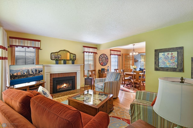 living room featuring a brick fireplace, light wood-type flooring, a textured ceiling, and an inviting chandelier