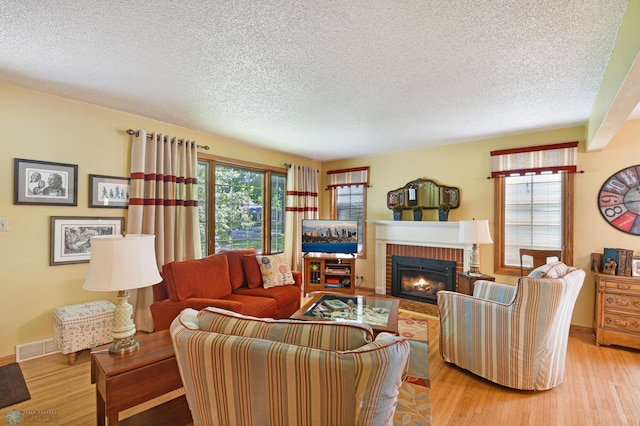 living room with a textured ceiling, a fireplace, light hardwood / wood-style flooring, and plenty of natural light