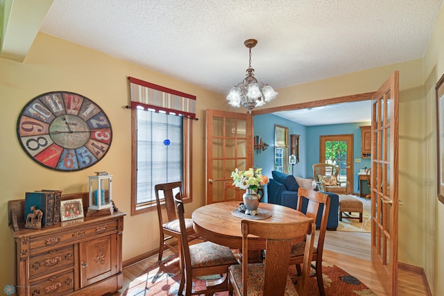 dining area with a textured ceiling, light hardwood / wood-style floors, an inviting chandelier, and french doors