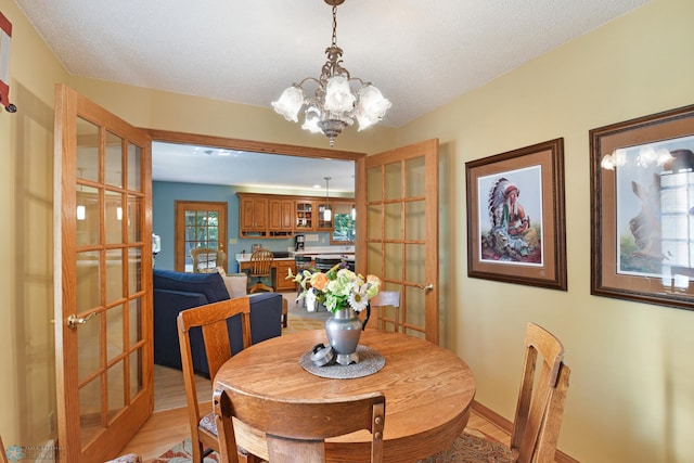 dining space with french doors, a textured ceiling, light hardwood / wood-style flooring, and a chandelier