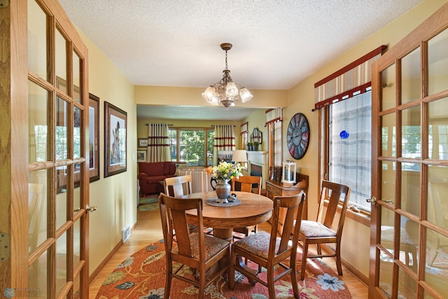 dining space with an inviting chandelier, light wood-type flooring, and a textured ceiling