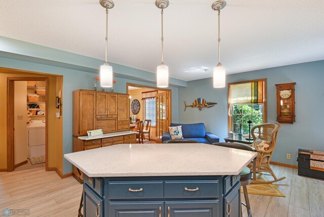 kitchen with light wood-type flooring, pendant lighting, a center island, and washer / dryer