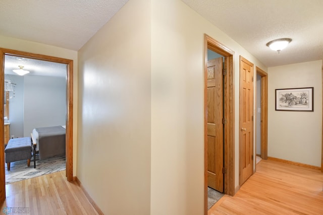 hall featuring light wood-type flooring and a textured ceiling