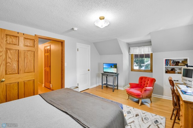 bedroom with a textured ceiling, light wood-type flooring, and lofted ceiling