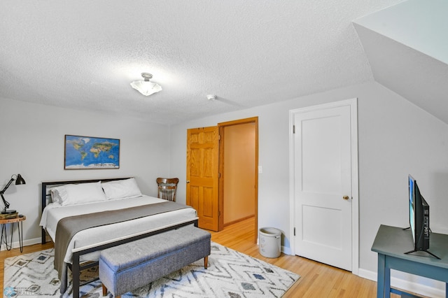 bedroom featuring a textured ceiling, light hardwood / wood-style flooring, and vaulted ceiling