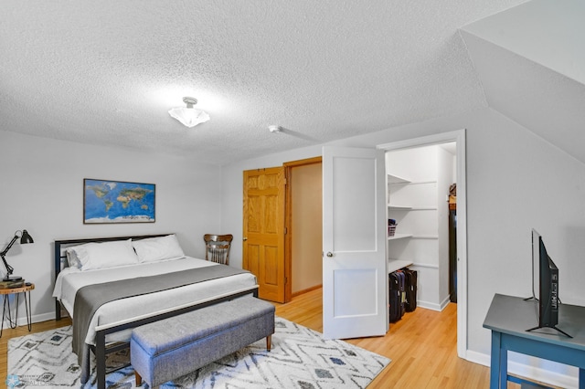 bedroom featuring light wood-type flooring, a textured ceiling, vaulted ceiling, and a walk in closet