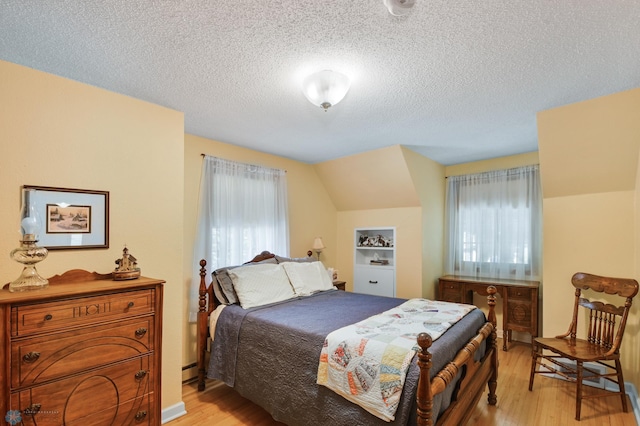 bedroom with a textured ceiling, light hardwood / wood-style flooring, vaulted ceiling, and multiple windows