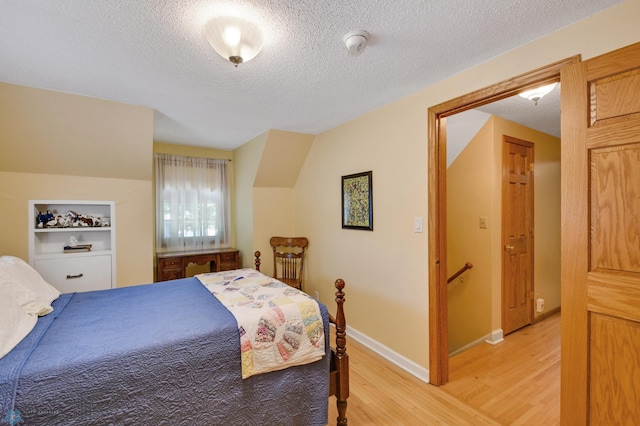 bedroom with a textured ceiling, vaulted ceiling, and light hardwood / wood-style flooring