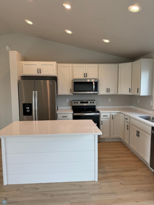 kitchen featuring white cabinetry, light hardwood / wood-style flooring, a kitchen island, appliances with stainless steel finishes, and vaulted ceiling