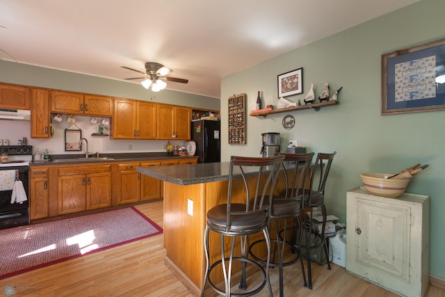 kitchen with electric range, light wood-type flooring, ceiling fan, black fridge, and sink