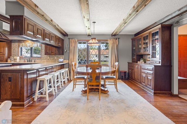 dining space with beamed ceiling, a textured ceiling, and hardwood / wood-style floors