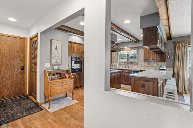 kitchen featuring light hardwood / wood-style floors, oven, beam ceiling, and a textured ceiling