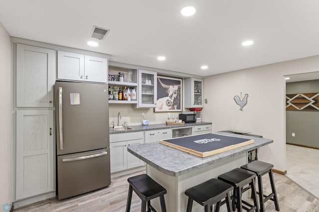 kitchen featuring a breakfast bar area, sink, light wood-type flooring, and stainless steel fridge