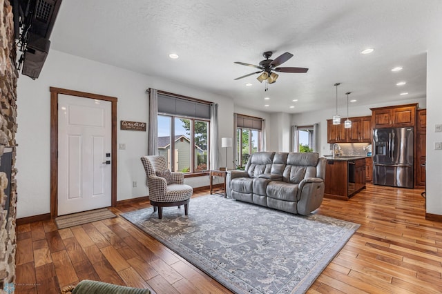 living room featuring ceiling fan, light hardwood / wood-style flooring, a textured ceiling, and sink