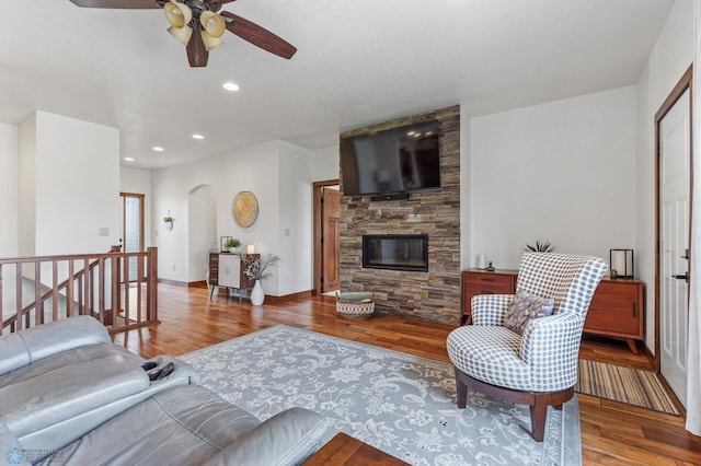 living room featuring ceiling fan, hardwood / wood-style floors, and a stone fireplace