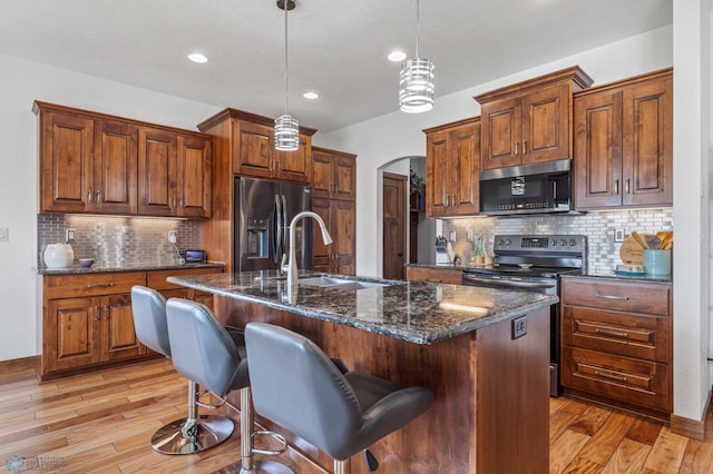 kitchen with a breakfast bar area, a kitchen island with sink, stainless steel appliances, and light hardwood / wood-style floors