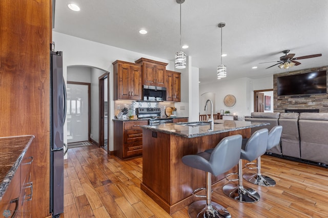 kitchen featuring sink, light hardwood / wood-style floors, dark stone counters, appliances with stainless steel finishes, and a center island with sink